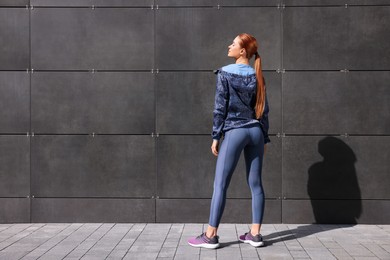 Photo of Beautiful woman in stylish gym clothes near dark grey wall on street, space for text