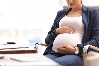 Photo of Young pregnant woman in suit at workplace, closeup. Space for text