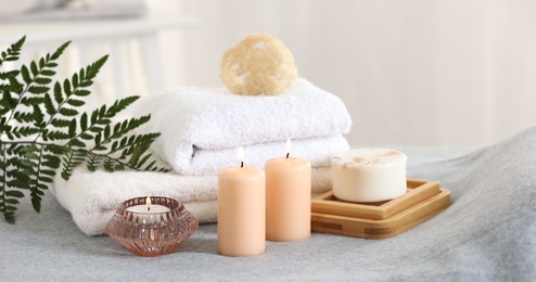 Photo of Spa composition. Burning candles, soap, towels and loofah on soft grey surface
