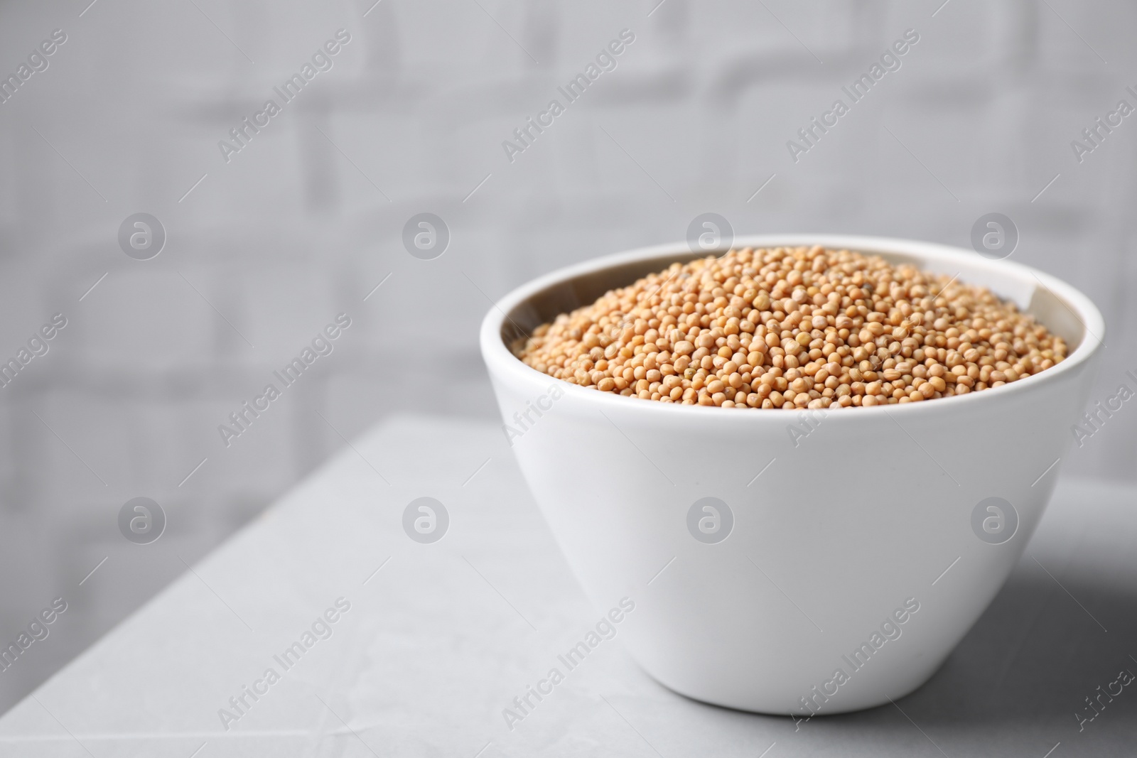 Photo of Mustard seeds in bowl on light table. Space for text