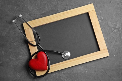 Photo of Stethoscope, heart and blackboard with space for text on gray background, top view. Cardiology concept