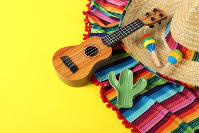 Photo of Composition with Mexican sombrero hat, ukulele and maracas on yellow table, closeup. Space for text