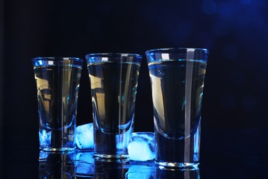 Photo of Alcohol drink in shot glasses and ice cubes on mirror surface, closeup