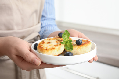 Photo of Woman with plate of delicious cottage cheese pancakes indoors, closeup