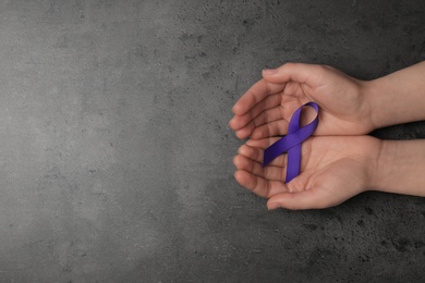Photo of Woman holding purple awareness ribbon on grey background, top view with space for text