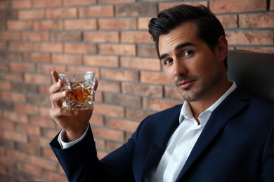 Photo of Young man with glass of whiskey near brick wall indoors