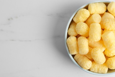 Photo of Bowl of delicious crispy corn sticks on white marble table, top view. Space for text