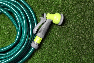 Photo of Watering hose with sprinkler on green grass, top view. Space for text
