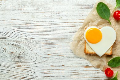Photo of Heart shaped fried egg with toast, spinach and tomatoes on white wooden table, flat lay. Space for text