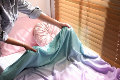Photo of Woman making bed with new colorful linens in children's room, closeup