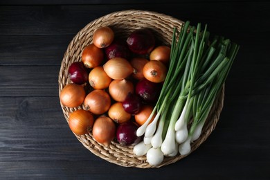 Photo of Wicker mat with different kinds of onions on black wooden table, top view