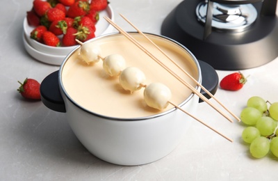 Photo of Pot with white chocolate fondue, dipped grapes and sticks on table
