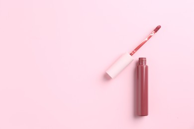 Photo of Bright lip gloss and applicator on pink background, top view. Space for text
