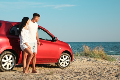 Photo of Happy couple near car on sandy beach, space for text. Summer trip
