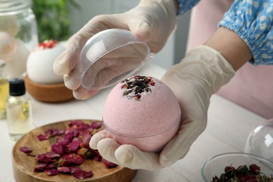 Photo of Woman in gloves with self made bath bomb at white table indoors, closeup