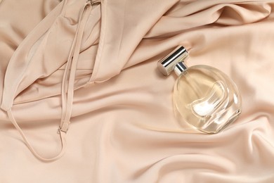 Photo of Luxury perfume in bottle on beige silk fabric, top view