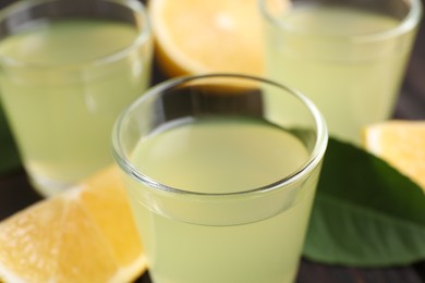 Photo of Tasty limoncello liqueur, lemon and green leaf on table, closeup
