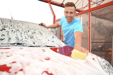 Photo of Young man cleaning vehicle with sponge at self-service car wash