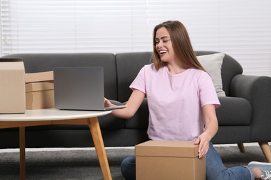 Photo of Happy woman using laptop while unpacking parcel at home. Online store