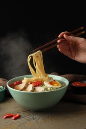 Photo of Woman eating delicious ramen with chopsticks at wooden table, closeup. Noodle soup