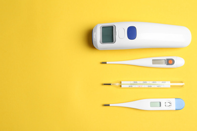 Different thermometers on yellow background, flat lay. Space for text