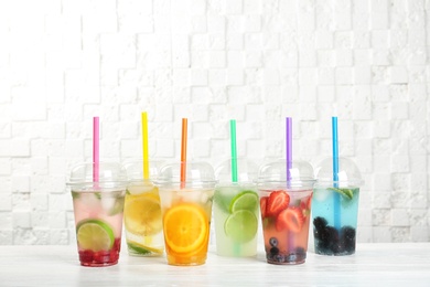 Photo of Plastic cups with lemonades on table near white wall