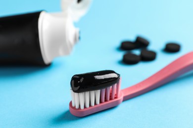 Photo of Brush with charcoal toothpaste on light blue background, closeup