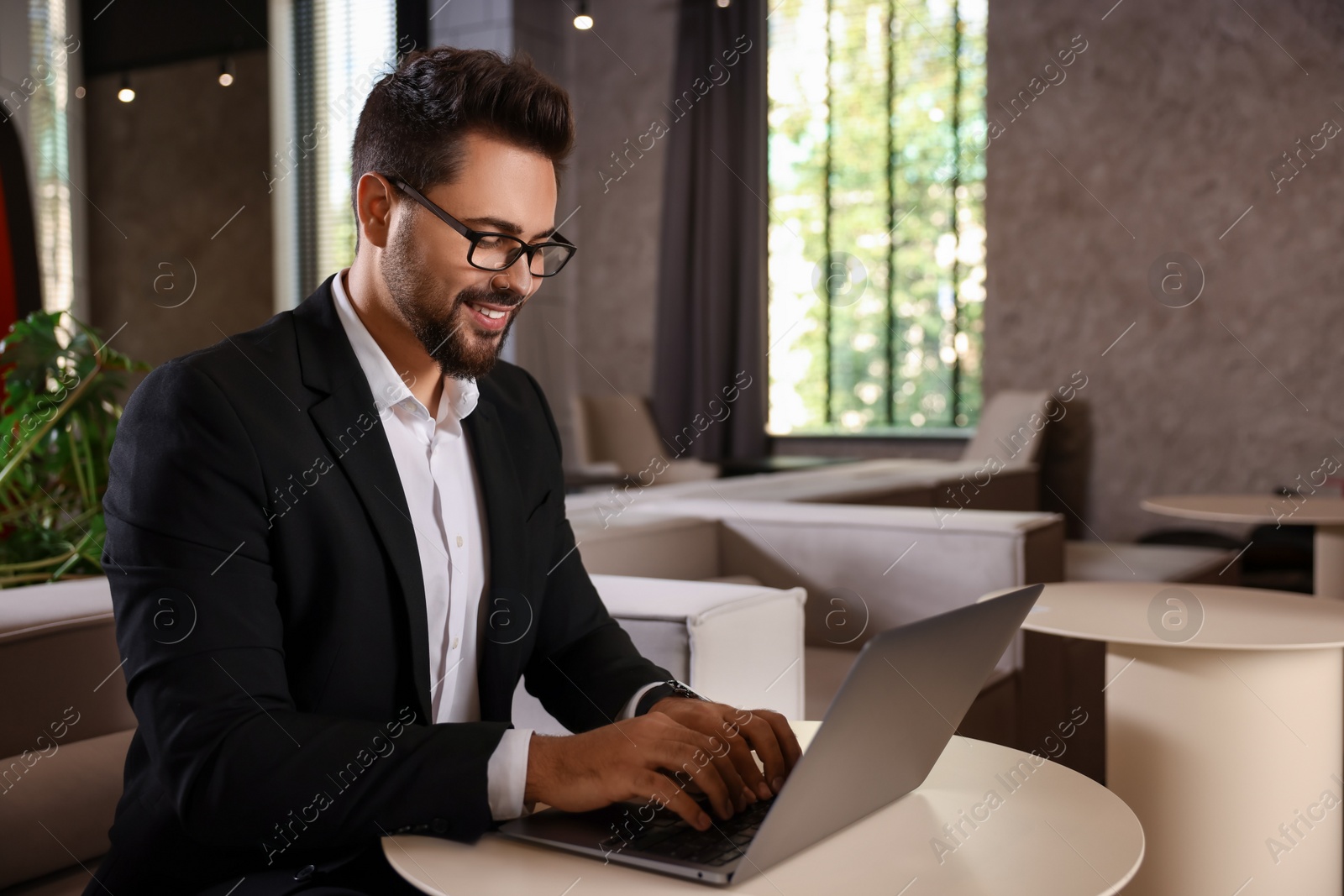 Photo of Happy young man with glasses working on laptop at table in office