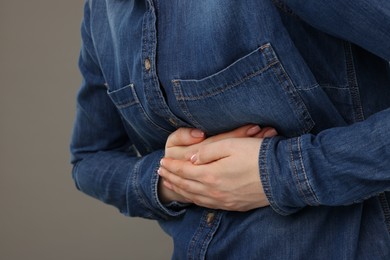 Photo of Woman suffering from stomach pain on grey background, closeup