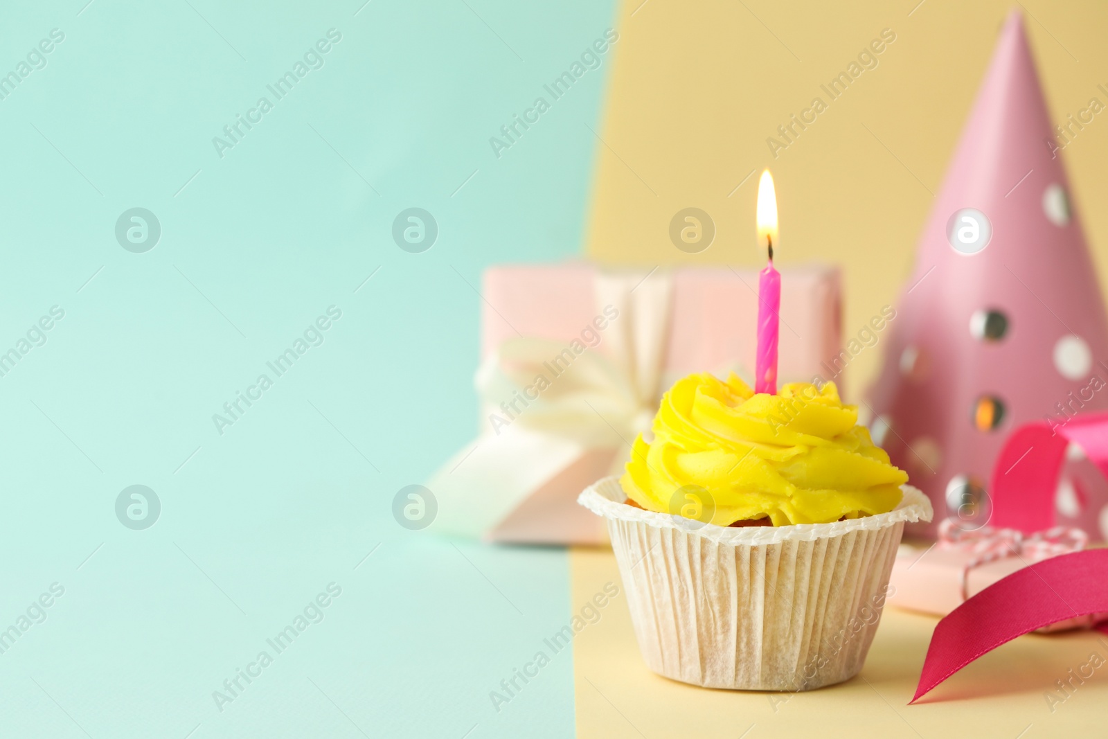 Photo of Tasty birthday cupcake with candle, gift box and party hat on colorful background. Space for text