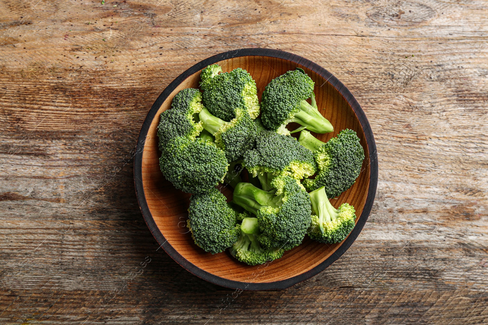 Photo of Wooden bowl of fresh broccoli on table, top view