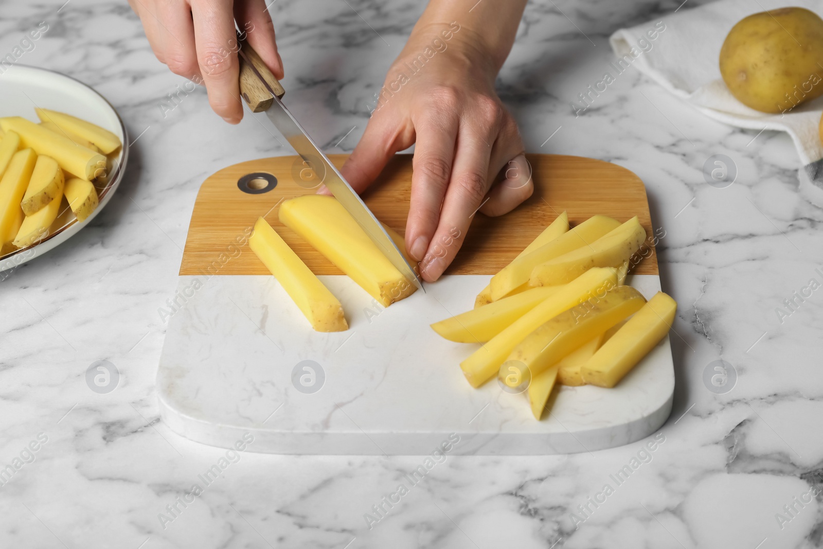 Photo of Woman cutting potato at white marble table, closeup. Cooking delicious French fries