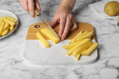 Photo of Woman cutting potato at white marble table, closeup. Cooking delicious French fries