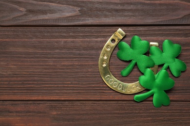 Photo of Clover leaves and horseshoe on wooden table, flat lay with space for text. St. Patrick's Day celebration