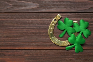 Clover leaves and horseshoe on wooden table, flat lay with space for text. St. Patrick's Day celebration