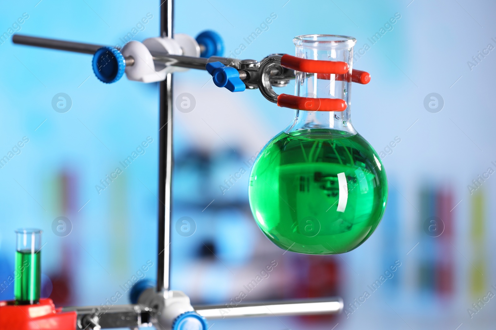 Photo of Flask with green liquid on retort stand in laboratory, closeup