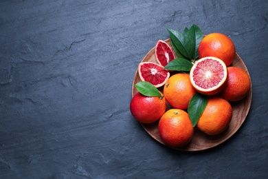 Plate of ripe red oranges and green leaves on dark table, top view. Space for text