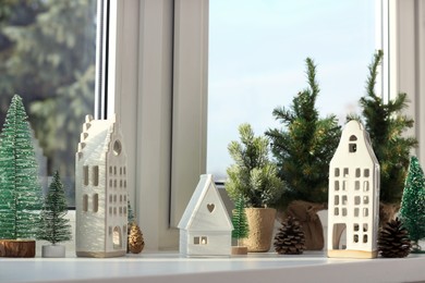 Photo of Beautiful house shaped candle holders and small fir trees on windowsill indoors