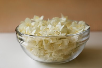 Photo of Beautiful jasmine flowers in glass bowl on white table, closeup