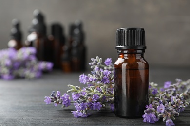 Photo of Bottle with natural lavender oil and flowers on wooden table against grey background, closeup view. Space for text