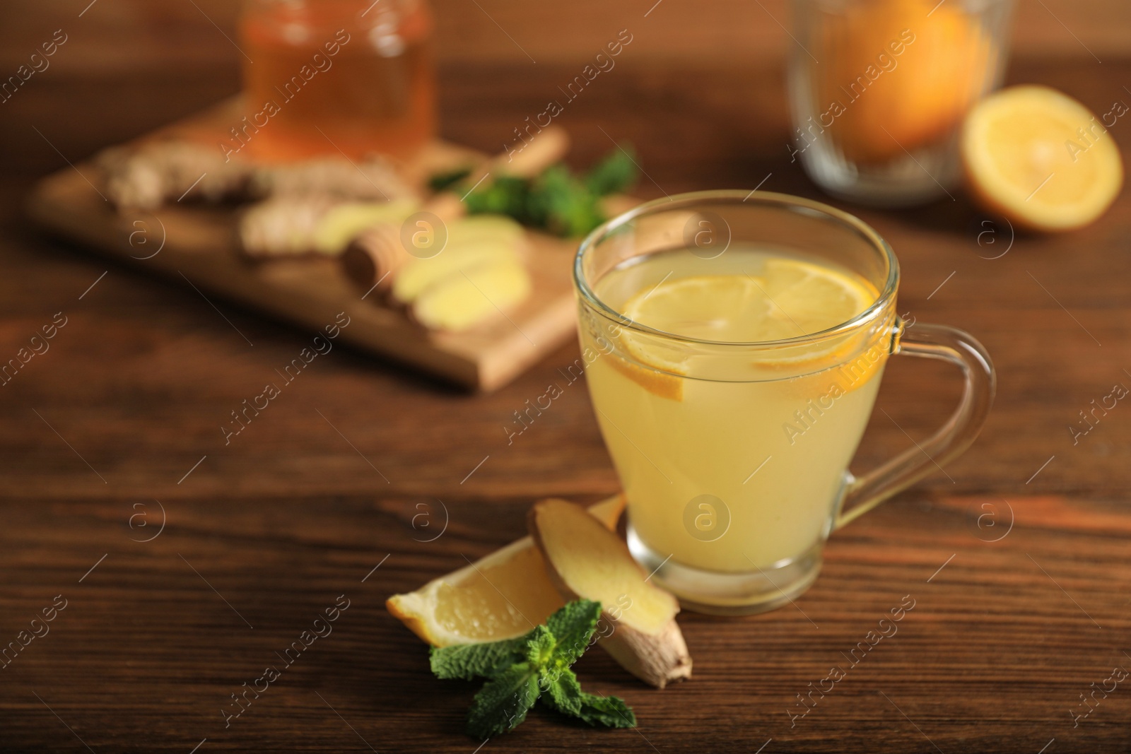 Photo of Glass of aromatic ginger tea and ingredients on wooden table, space for text