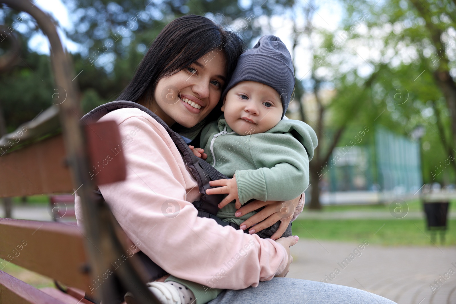 Photo of Mother holding her child in sling (baby carrier) on bench in park