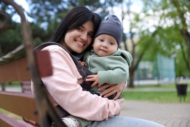 Mother holding her child in sling (baby carrier) on bench in park