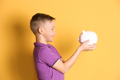 Photo of Little boy with piggy bank on color background