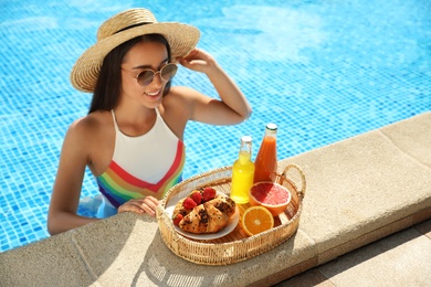 Young woman with delicious breakfast on tray in swimming pool