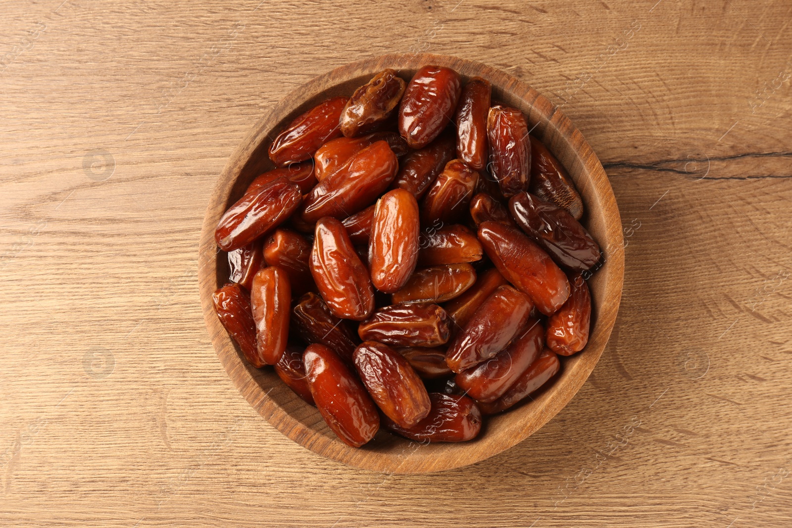 Photo of Tasty sweet dried dates in bowl on wooden table, top view