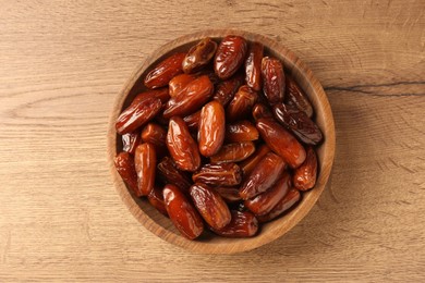 Photo of Tasty sweet dried dates in bowl on wooden table, top view