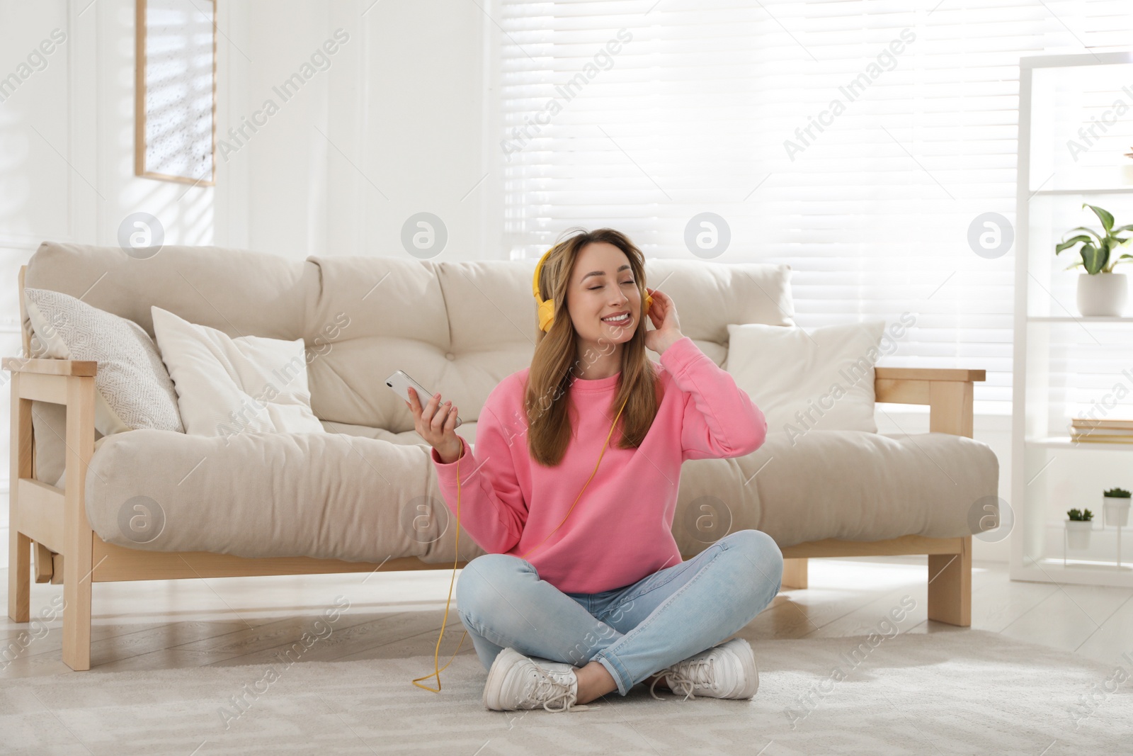 Photo of Young woman with headphones listening to music while sitting on floor in living room