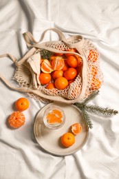 Photo of Delicious ripe tangerines, glass with sparkling wine and fir branch on white bedsheet, flat lay