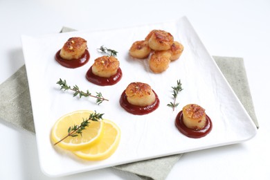 Photo of Delicious fried scallops with tomato sauce and lemon served on white table